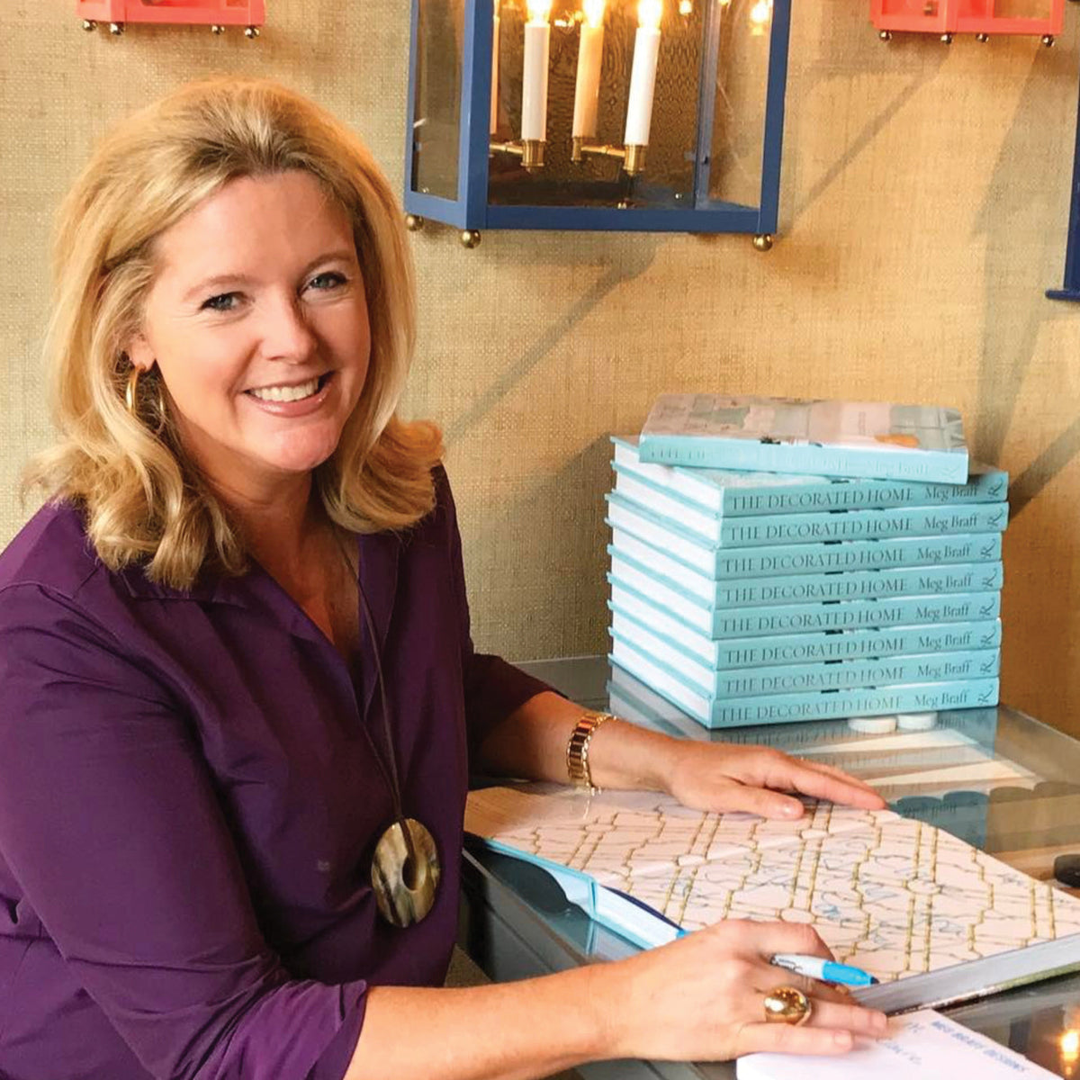A smiling woman signs The Decorated Home at a glass table, embodying Tuckernuck's classic, effortless, and fun high-end style.