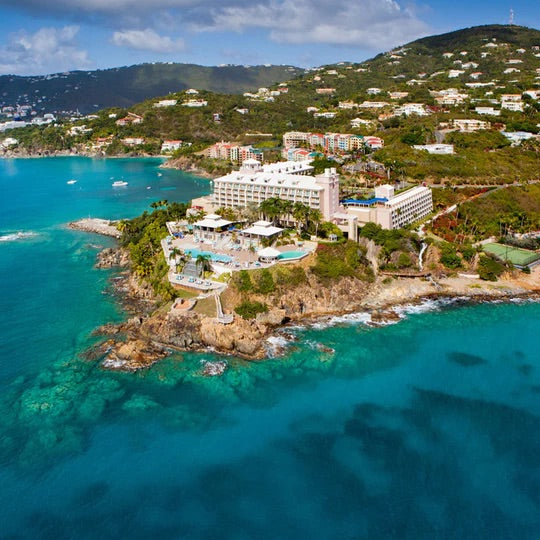 Aerial view of a classic, high-end coastal resort with an infinity pool, nestled on a rocky promontory, offering effortless access to fun, turquoise waters.