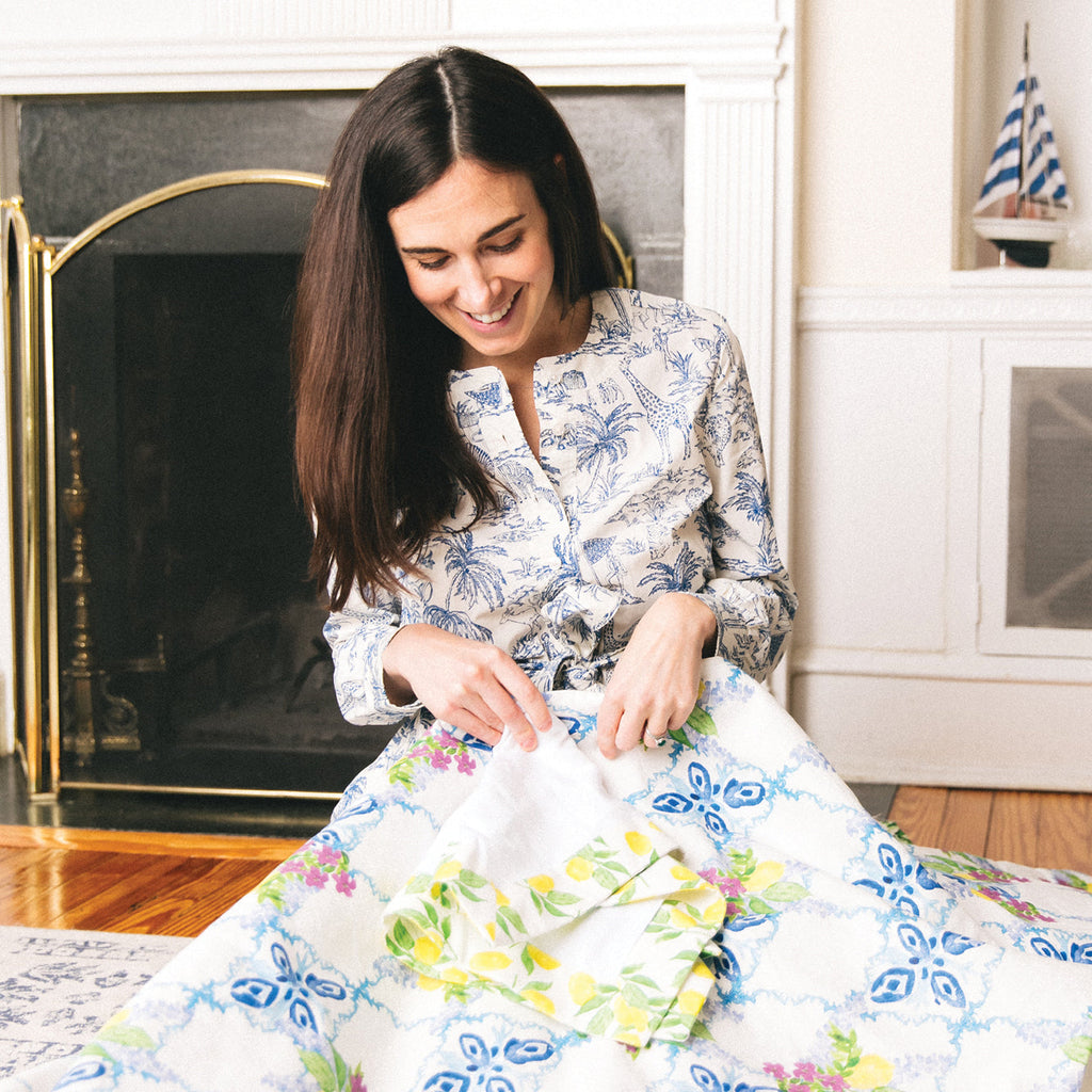 Woman smiling, examining a large, brightly patterned fabric in a living room, embodying classic, effortless style with a fun, high-end design.