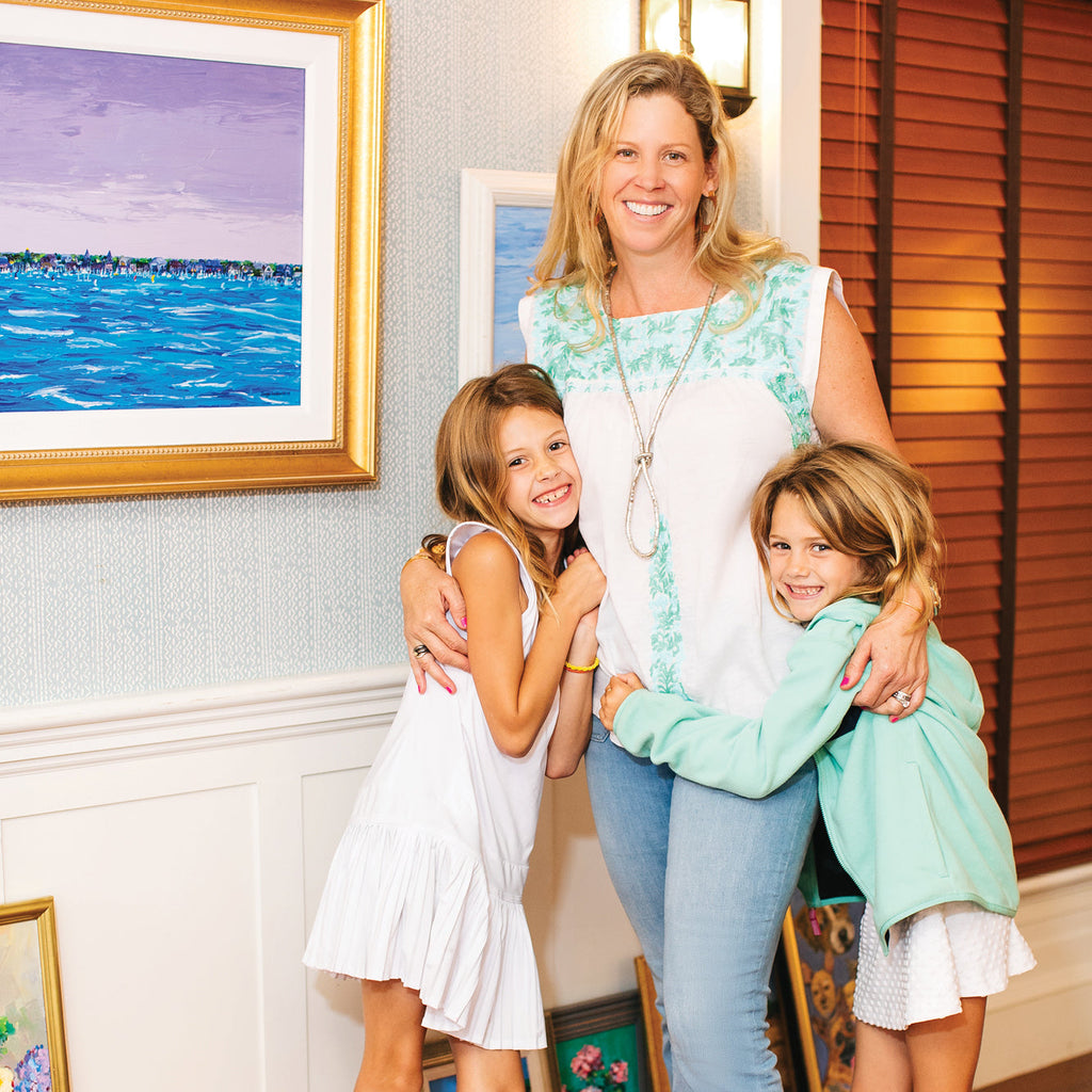 A smiling mom with two daughters embraces indoors, exuding a classic, effortless, and fun vibe, reflecting Tuckernuck's high-end, family-friendly aesthetic.
