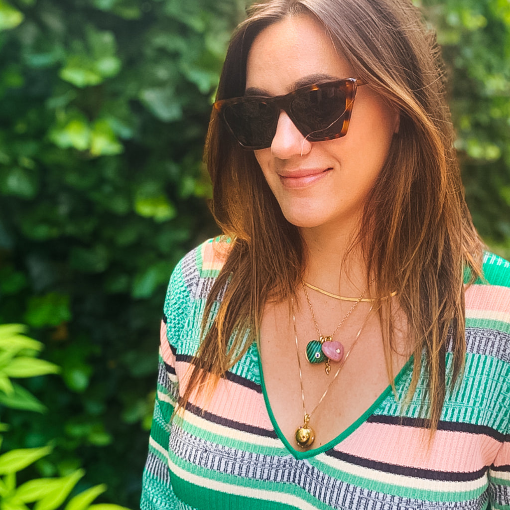 Person wearing a classic striped knit top and tortoiseshell sunglasses, accessorized with three effortless gold necklaces, exuding a fun, high-end garden style.