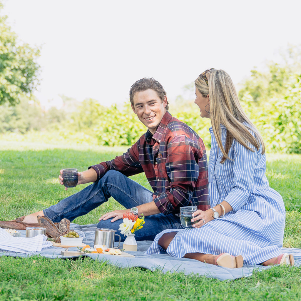 A young couple enjoys an effortless, fun picnic with classic cheese, fruit, and flowers, embodying Tuckernuck's high-end, confident lifestyle.