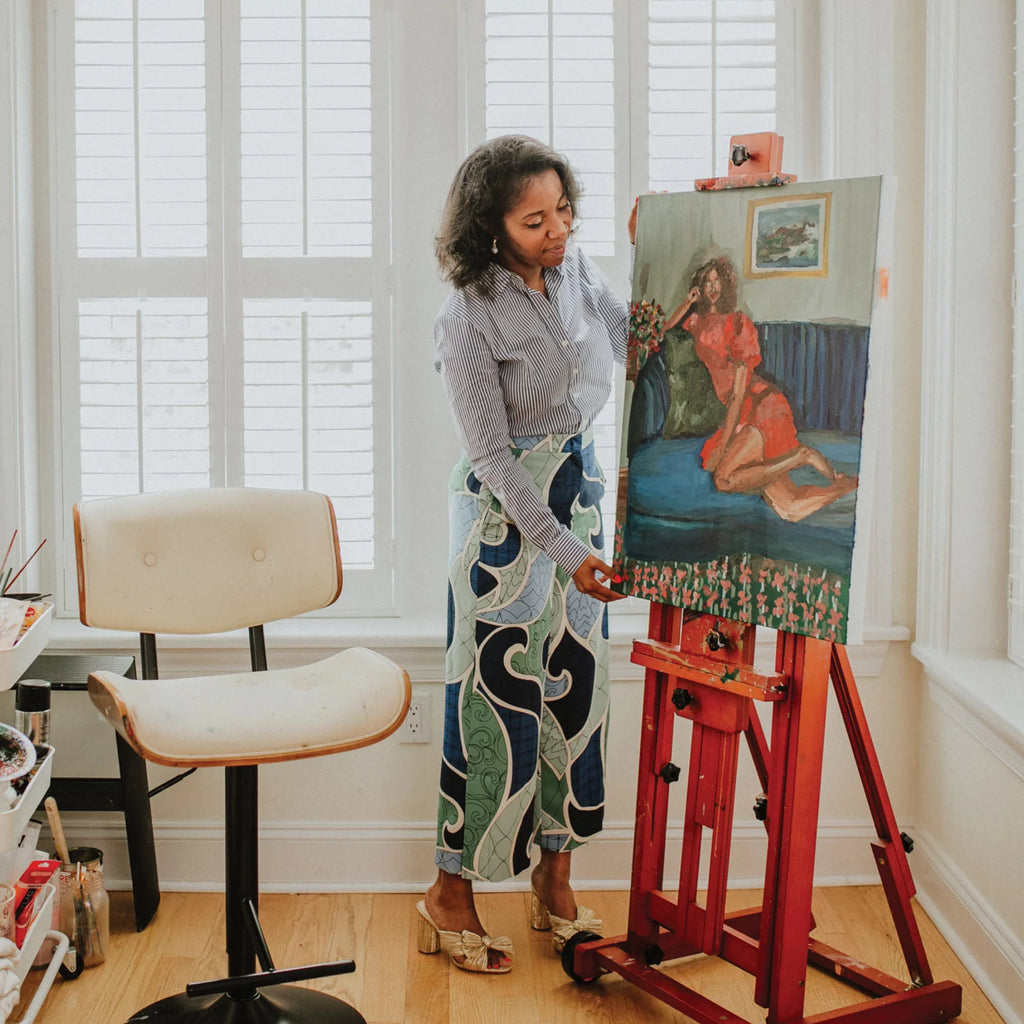 A woman in a classic striped blouse and patterned skirt paints a colorful portrait, exuding effortless style in a bright, fun, high-end studio.