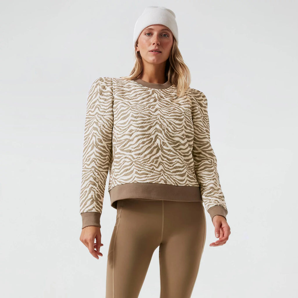 Model in classic beige-and-white zebra-stripe sweatshirt with puffed shoulders, taupe leggings, and a white beanie for an effortless, fun, high-end look.