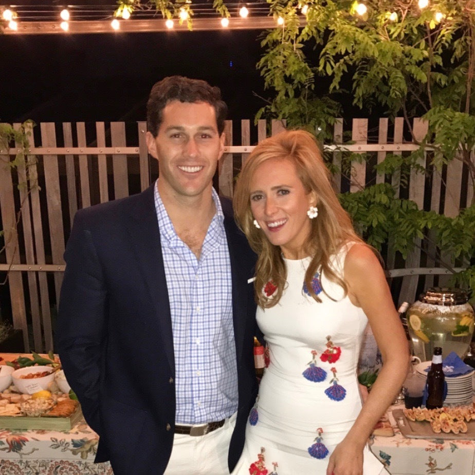 A man and woman in classic, high-end attire enjoy an effortless, fun gathering with appetizers and drinks under string lights in an elegant outdoor setting.