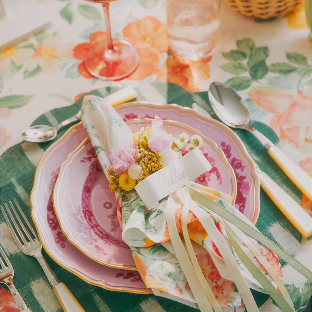 Elegant, classic place setting with pink floral plates, coordinating napkin, and ivory cutlery; features include a Charlie place-card and fresh blooms, exuding effortless, high-end charm.