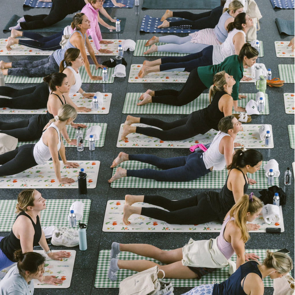 Overhead view of a classic, high-end yoga class with young women in back-bending poses on patterned mats, embodying effortless fun and confidence.