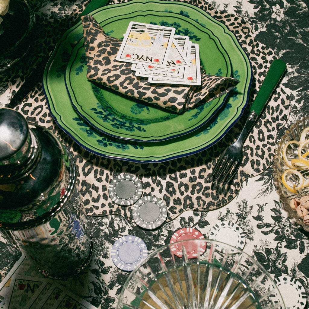 Effortlessly chic tabletop with floral plates, leopard napkin, NYC playing cards, poker chips, metal shaker, and cut-glass tumbler on animal-print cloth.