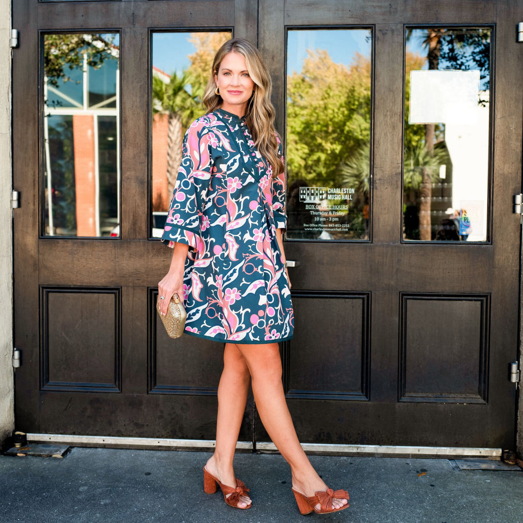 Woman in a classic floral dress with gold clutch and brown mules outside Charleston Music Hall, embodying effortless, high-end style with a fun, confident flair.