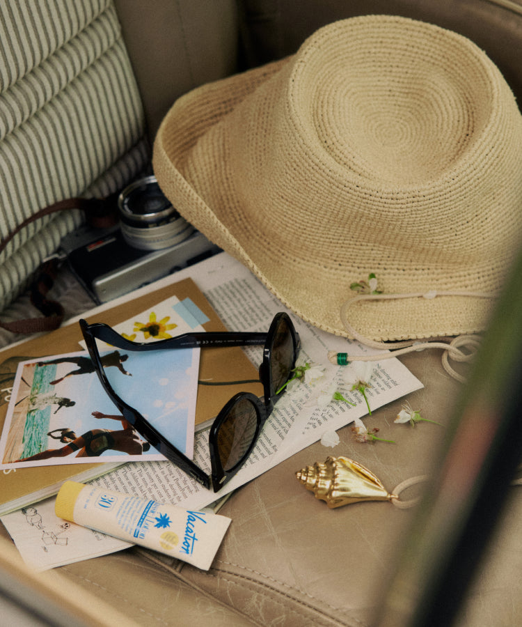 A chair covered in a straw hat, sunglasses, and other summer mementoes.