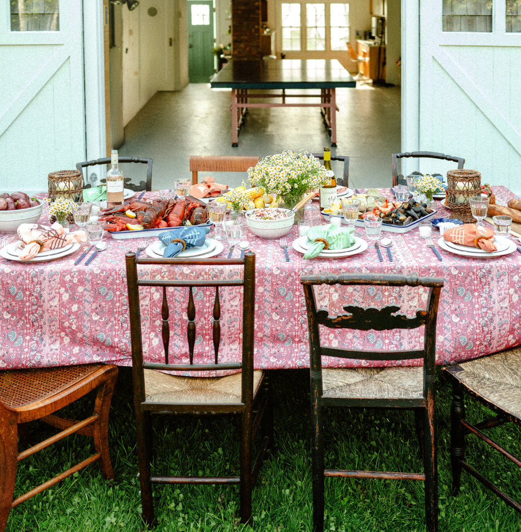 A summer table of corn, lobster, clams, and shrimp featuring a red tablecloth and colorful napkins.