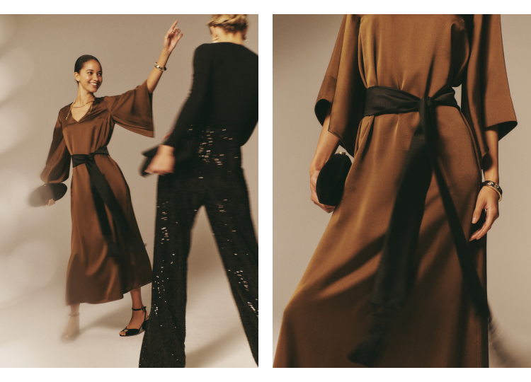 Image one: Two women standing in a studio. One woman is wearing a brown long-sleeved maxi dress with a black belt and the other is wearing a black sweater and black sequined pants. Image two: close up of woman in a brown long-sleeved maxi dress with a black sash.