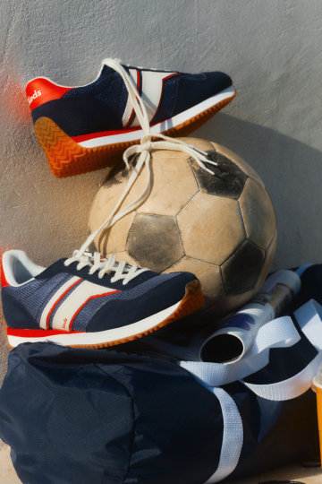 A pair of navy sneakers resting on a soccer ball and navy duffle bag.