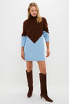A woman wears a Hyacinth House brown and light blue turtleneck mini sweater dress with long sleeves, styled with knee-high brown suede boots.