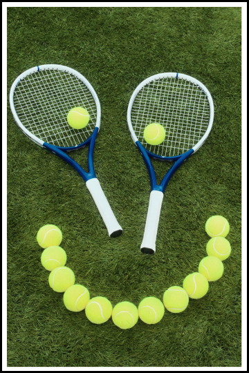 A smiley face made with tennis balls and two tennis rackets.