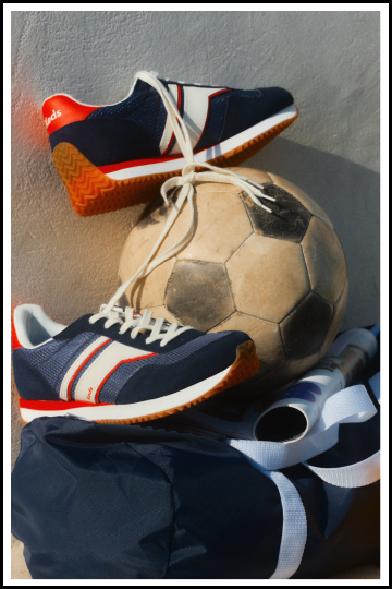 A pair of navy tennis shoes around a soccer ball.
