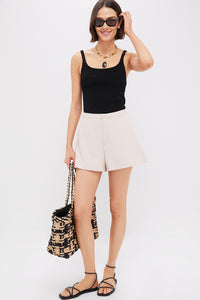 A woman in a black tank top, Hyacinth House Beige Hallie Shorts, black sandals, sunglasses, necklace, and patterned tote bag shows off an essential warm-weather look against a plain white background.