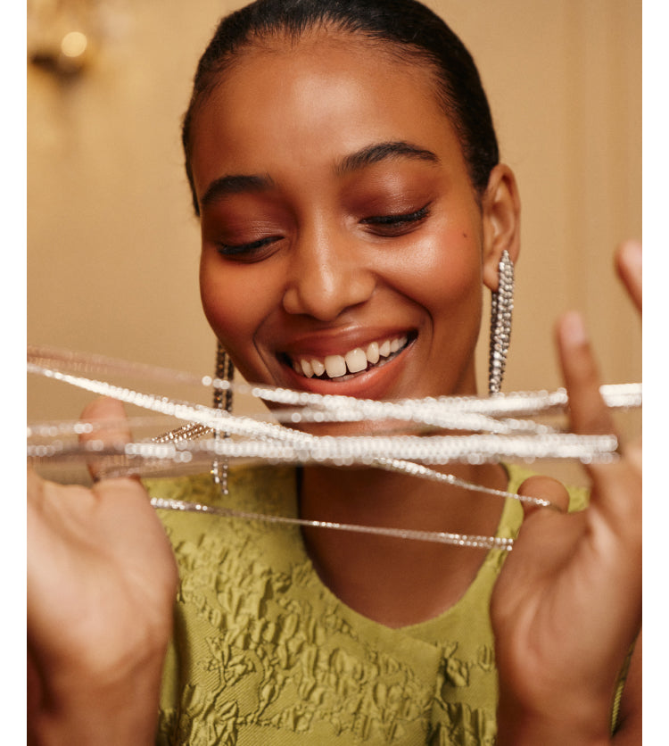 A woman wearing a green jacquard top and silver earrings, holding silver tinsel.