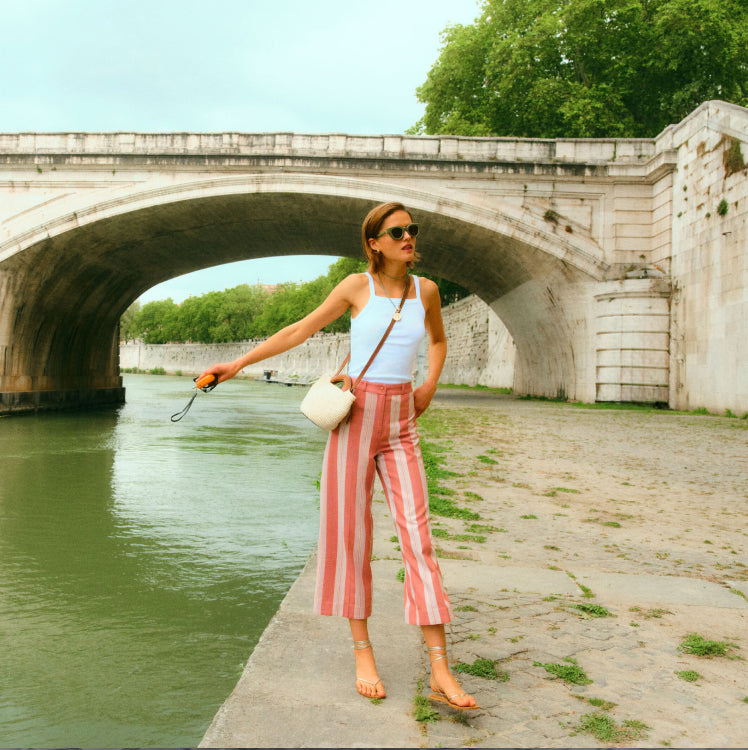 Woman standing under a bridge in red and white striped pants and a white tank.