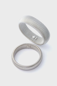 Two silver alloy bangles with ribbed designs are shown, one upright and one flat. These Ben Amun Silver Cobra Bracelets showcase elegant craftsmanship and make bold statement jewelry pieces.