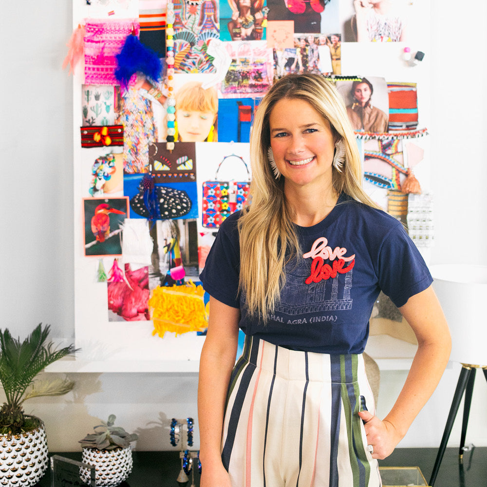 Smiling woman in a navy tee with love love patch and striped pants in a creative workspace, embodying classic and effortless Tuckernuck style.