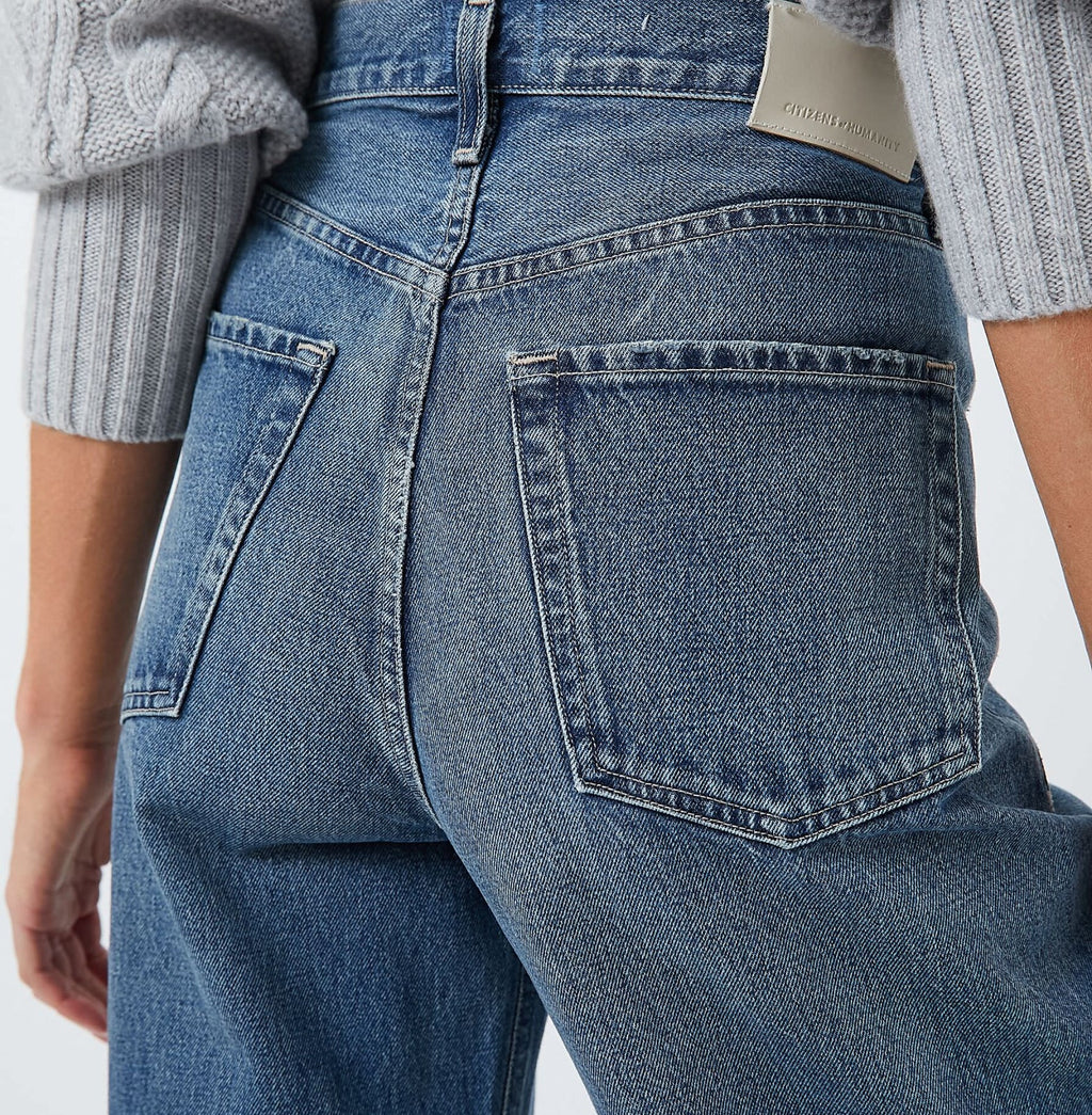 Close-up of high-waisted blue denim jeans with patch pockets and leather patch, paired with a light gray cable-knit sweater, showcasing classic, effortless style.