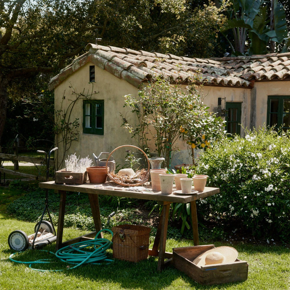 Sunlit garden area with classic terracotta pots, effortless gardening tools, and a wicker hamper, reflecting Tuckernuck's fun, high-end lifestyle.