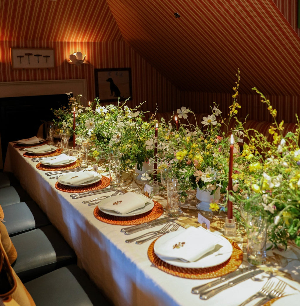 A classic, high-end dining setup in an attic-style room, featuring effortless, fun decor with wildflowers, red candles, and elegantly arranged place settings.