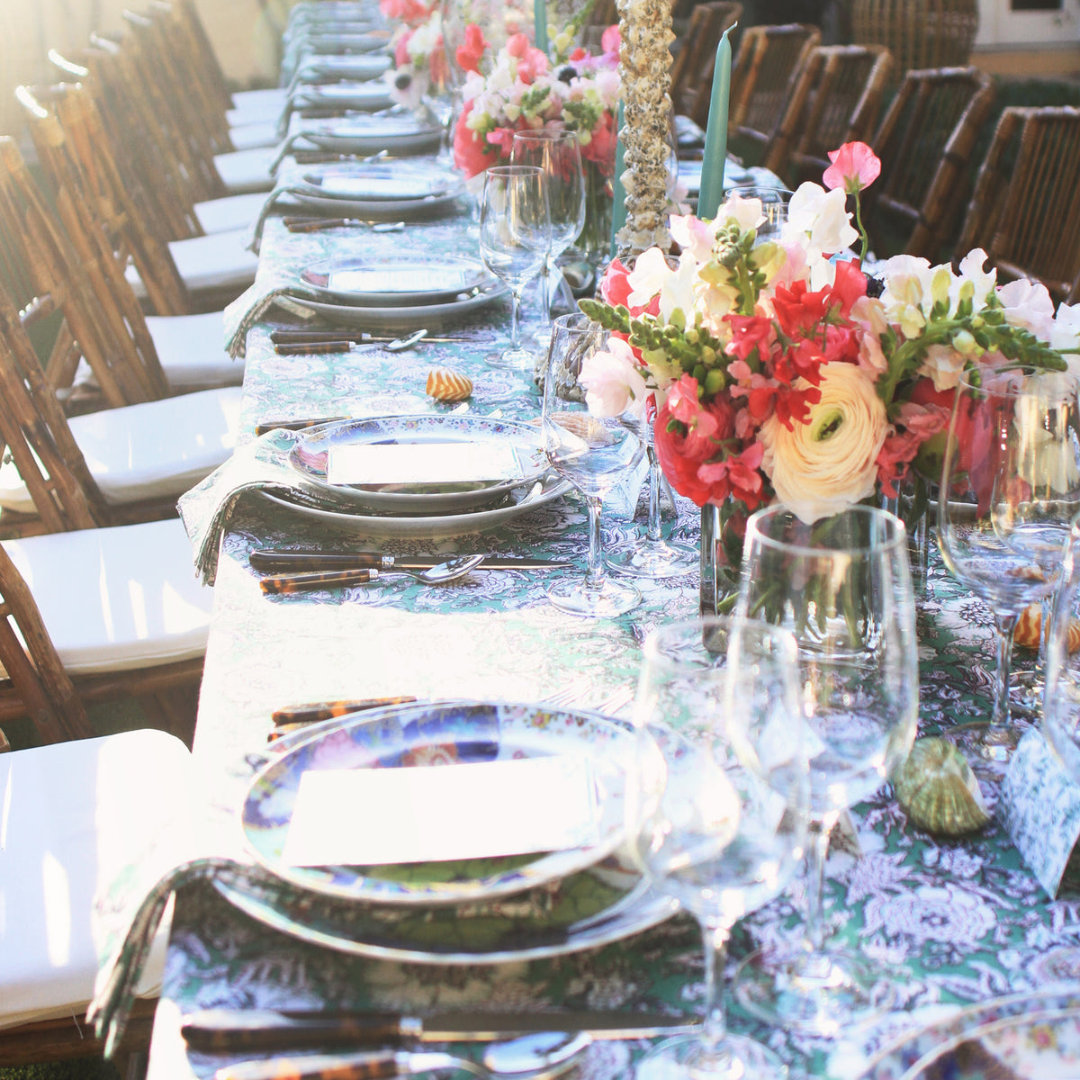 A classic, high-end dining table set for an effortless garden party, featuring elegant floral arrangements, patterned tablecloth, and bamboo-style chairs with a fun, inviting ambiance.
