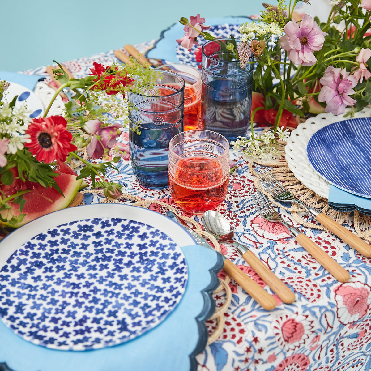 Effortless, classic table setting with a blue-and-white plate, wooden utensils, floral accents, and vibrant drinks, embodying a fun, high-end Tuckernuck style.