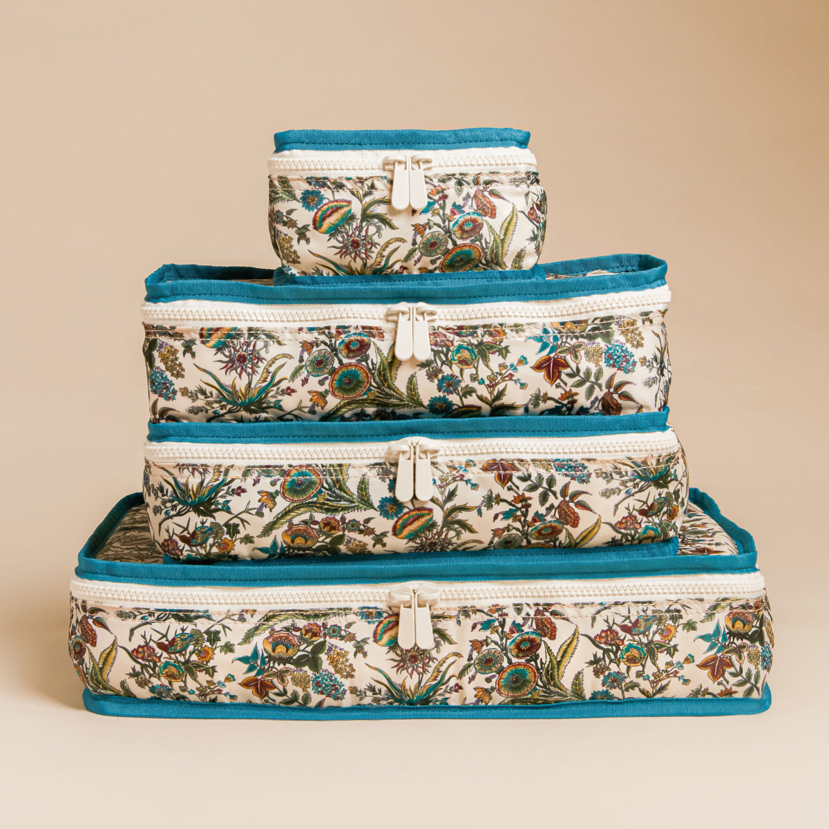 A stack of four classic, floral-botanical print zip-top storage pouches with teal trim, exuding an effortless, high-end style for fun, organized travel.