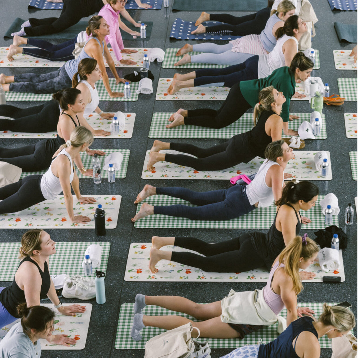 Overhead view of a classic, high-end yoga class with young women in back-bending poses on patterned mats, embodying effortless fun and confidence.