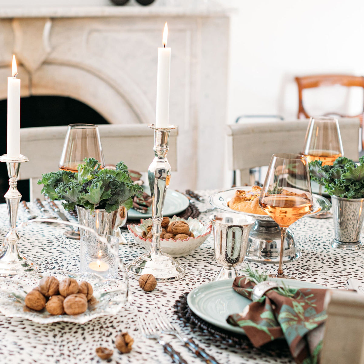 An elegantly set dining table with classic silverware, effortless kale centerpieces, fun patterned tableware, and high-end glassware, capturing a sophisticated, intimate gathering.