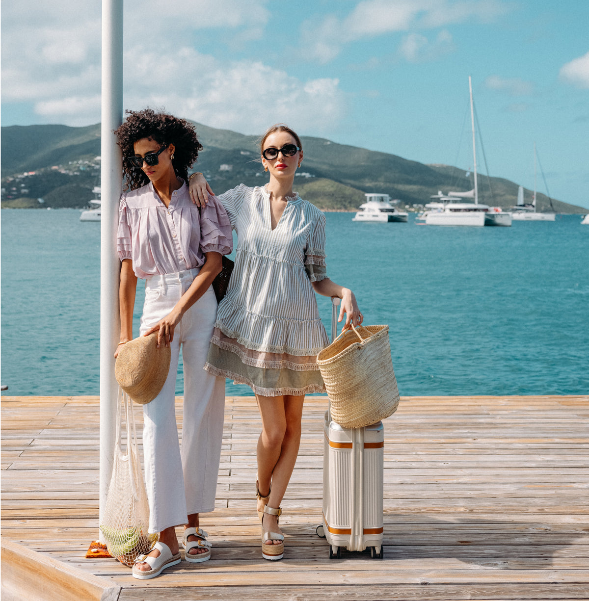 Two women in classic, effortless summer attire stand on a dock by a marina, embodying Tuckernuck's fun, high-end style with chic accessories.