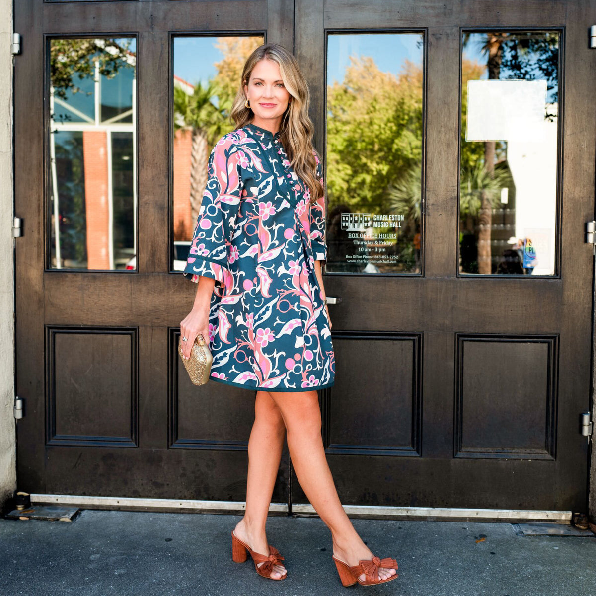 Woman in a classic floral dress with gold clutch and brown mules outside Charleston Music Hall, embodying effortless, high-end style with a fun, confident flair.