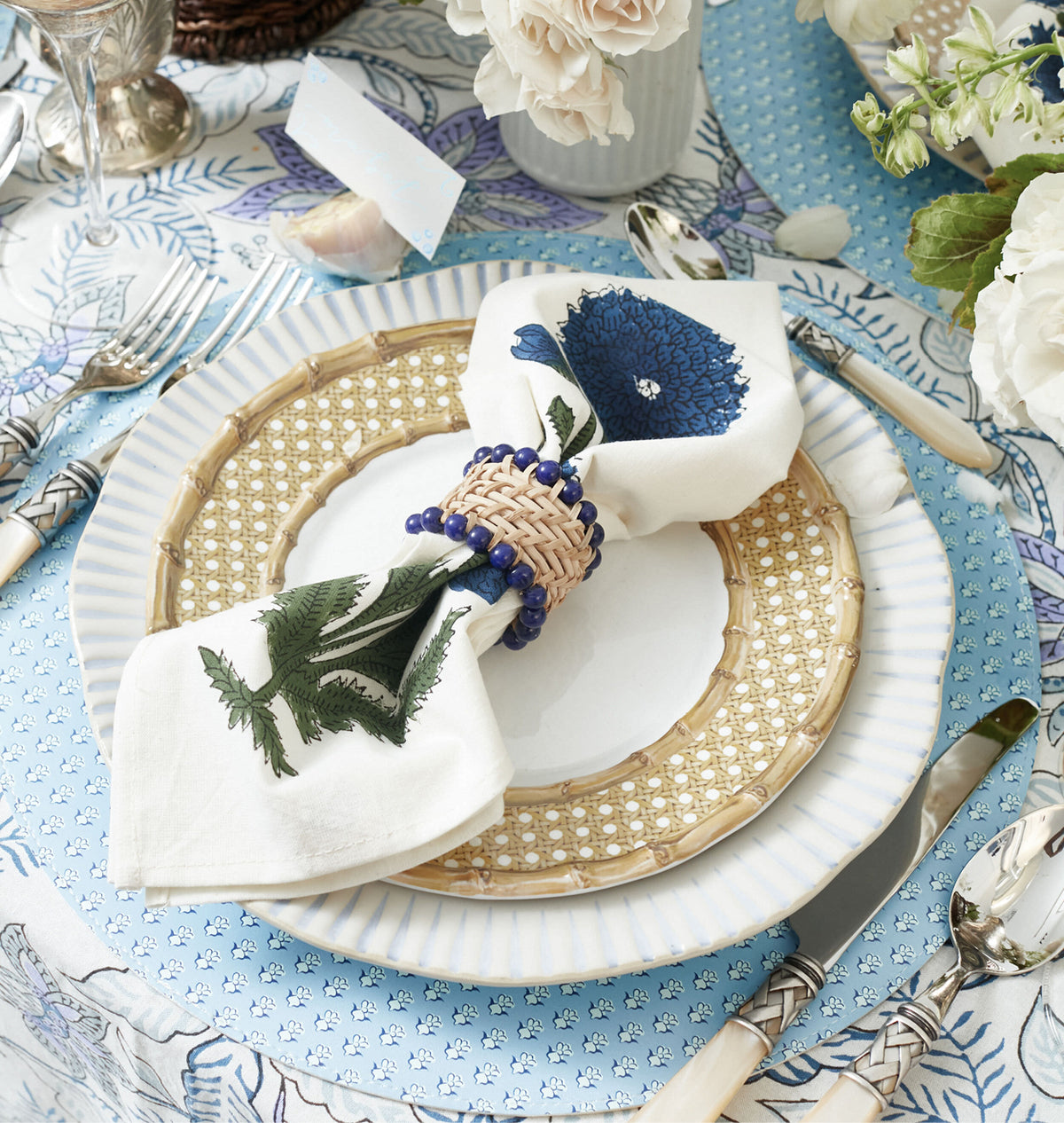 Classic, effortless place setting with floral tablecloth, woven accents, and elegant cutlery, embodying high-end, fun style with blue, green, and neutral tones.