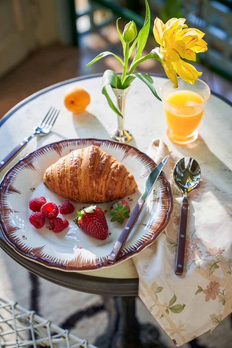 Elegant breakfast scene featuring Rose Trellis Printed Napkins. Classic floral design complements a croissant, berries, and juice, reflecting Tuckernuck's effortless, high-end style.