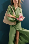 Woman wearing a green dress holds pink flowers, showcasing the classic, high-end Natural Crochet Raffia Willow Tote Bag, effortlessly chic with a relaxed, fun silhouette.