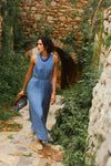Woman in a long sleeveless blue dress and a beaded necklace. 