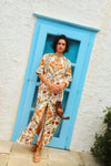Woman standing in front of a blue door in a long, floral printed caftan with tan leather sandals.