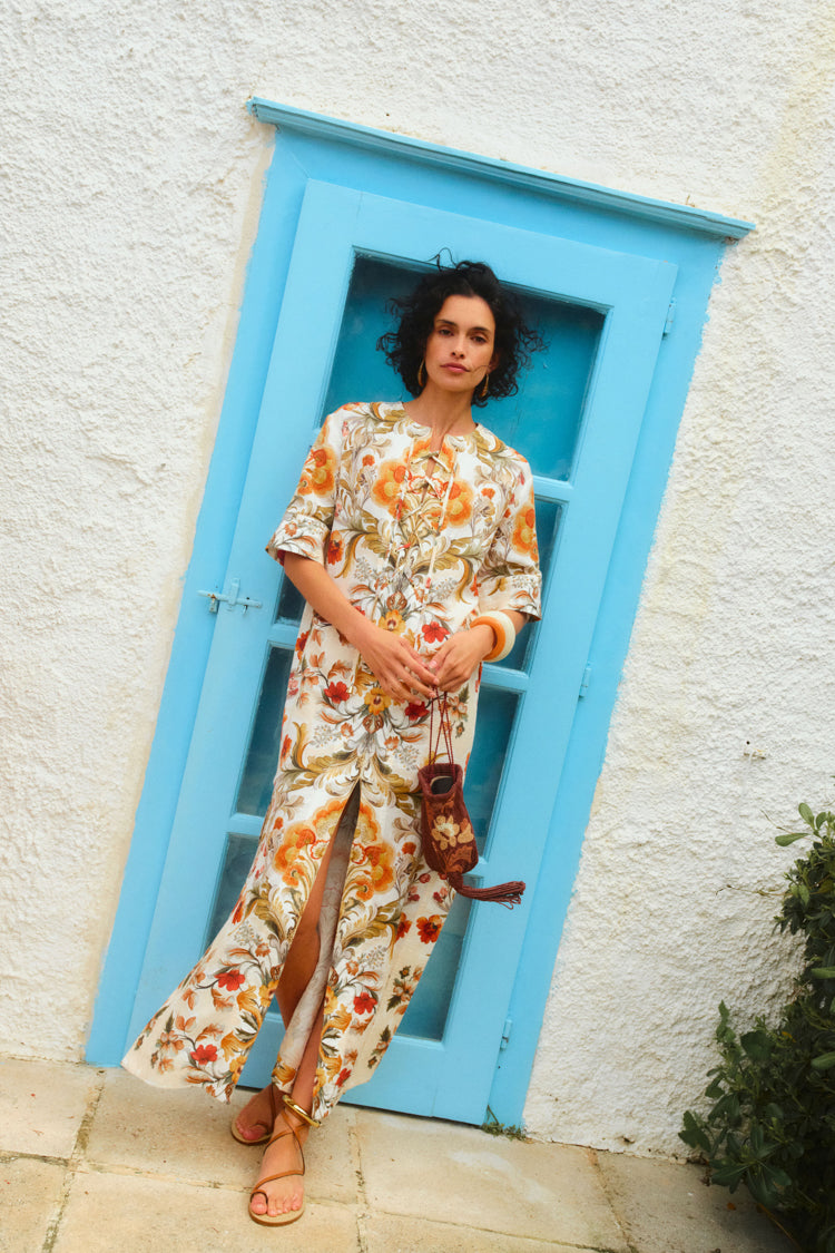 Woman standing in front of a blue door in a long, floral printed caftan with tan leather sandals.