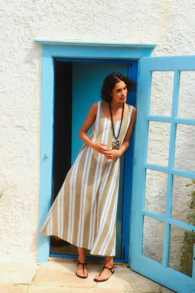 Woman standing in a blue doorway in a long tank dress with blue, white, and brown stripes. 