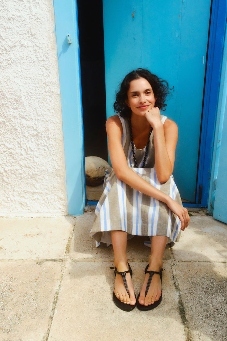 Woman sitting in a doorway wearing a long dress with blue, brown, and white stripes. 