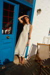 Woman standing in front of a blue door in a white dress with blue trim. 