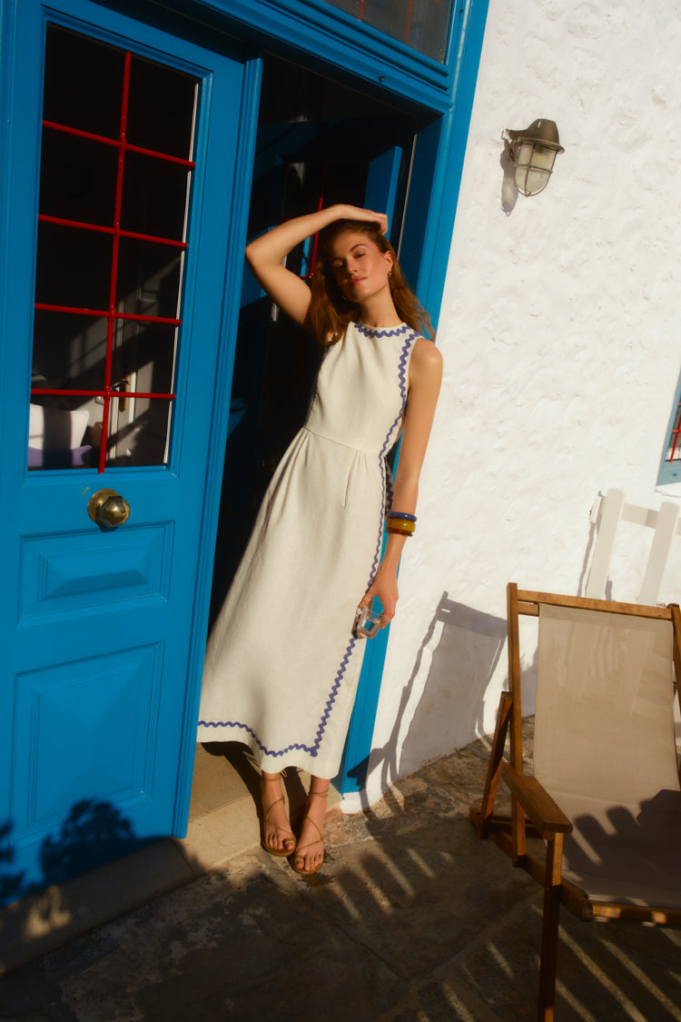 Woman standing in front of a blue door in a white dress with blue trim. 