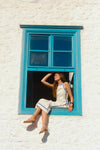 Woman sitting on a blue windowsill in a white dress with blue trim. 