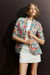 Woman standing in front of a dark backdrop in a madras blazer and a white dress. 