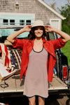 Woman standing in front of a vintage Wagoneer in a straw hat, red button down, and red, white, and blue stripe dress. 