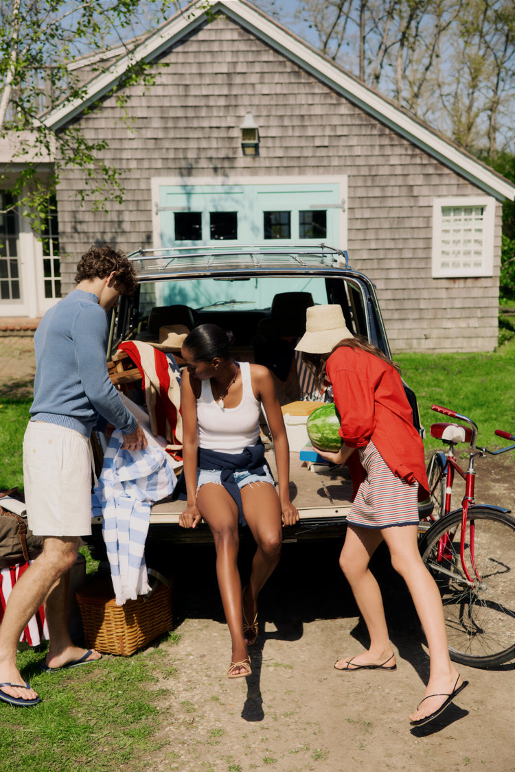 Three people packing up the back of a Wagoneer in front of a brown shingled house. 