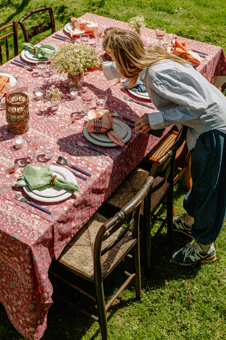Woman setting an outdoor table with a red tablecloth and colorful napkins. 